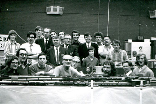 Around twenty members young and old posing for a photograph behind small model railway locomotives