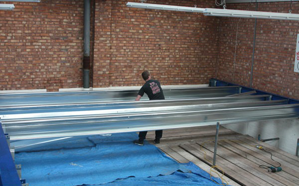 A man is working to install metal crossbeams spanning between two brick walls
